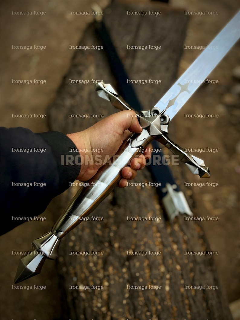 K&ouml;nnte beinhalten: Ein silbernes Schwert mit kreuzf&ouml;rmigem Knauf wird gehalten. Die lange, reflektierende Klinge hat eine Hohlkehle. Der Knauf hat ein Sterndesign. Der Text "Ironsaga forge" ist als Wasserzeichen zu sehen. Die Gesamtl&auml;nge des Schwertes betr&auml;gt ca. 76 cm.