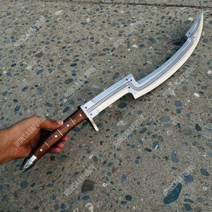 May include: A curved, silver-colored blade with a wooden handle. The blade features decorative star and line patterns. The handle is brown with silver accents. The knife is held by a person's hand.