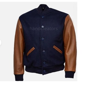 Könnte beinhalten: Marineblaue Collegejacke mit braunen Lederärmeln. Die Jacke hat eine Knopfleiste, zwei Vordertaschen und einen gerippten Kragen und Bündchen. Der Text "handcreators" ist auf der Vorderseite aufgedruckt.