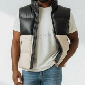 May include: A two-tone puffer vest in black and cream. The vest has a high collar and a zip-up front. The model is wearing a white t-shirt and blue jeans. The vest is a stylish outerwear option for cooler weather.