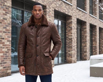 May include: A brown leather coat featuring a thick, dark brown shearling collar and interior lining. The coat includes a button-front closure, two front flap pockets, and quilted shoulder detailing, providing a structured look for cold weather.