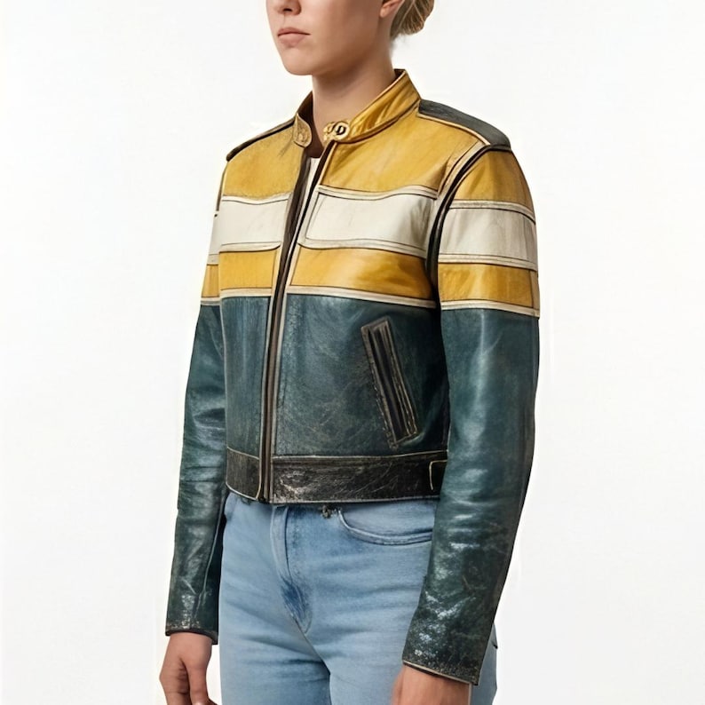 Op de afbeelding: Een leren jack met kleurvlakken, bestaande uit een mosterdgeel bovendeel, een horizontale witte streep en een donkergroenblauw onderstuk. Het jack heeft een opstaande kraag met een goudkleurige metalen sluiting, een ritssluiting en twee zijzakken.