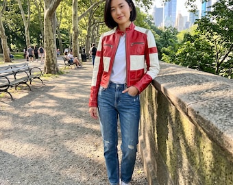 Op de afbeelding: Een rood en wit color-block leren jack met een opstaande kraag, zilverkleurige ritssluitingen en lange mouwen, gedragen over een effen wit t-shirt met een blauwe spijkerbroek met lichte slijtageplekken en witte canvas sneakers.