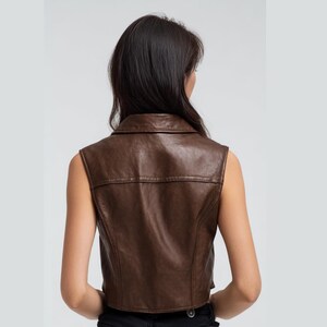 Peut inclure: Un gilet en cuir marron avec un col. Le gilet sans manches a une coupe ajust&eacute;e et des d&eacute;tails de couture visibles. La vue arri&egrave;re montre un design classique, adapt&eacute; pour &ecirc;tre superpos&eacute; ou port&eacute; seul.