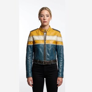 Op de afbeelding: Een leren jas met een mosterdgeel bovenstuk bij de borst en schouders, een horizontale witte streep en een blauw onderstuk. De jas heeft een opstaande kraag met drukknoopsluiting, een ritssluiting aan de voorzijde, schouderkleppen en een donkerbruine riem.