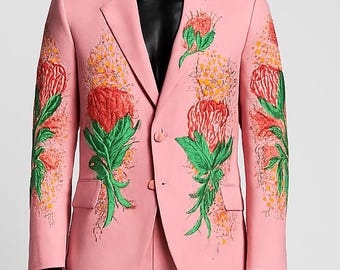 以下が含まれることがあります： 赤、緑、黄色で刺繍された花の模様が特徴の、明るいピンク色のスーツ。 黒いマネキンに着せられた、ブレザーとマッチするパンツのセットです。 花の刺繍がデザインの重要な要素です。