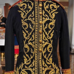 May include: A black jacket with ornate gold embroidery, featuring a high collar and gold buttons. The cuffs and collar are trimmed with red and gold detailing. This garment is likely a historical or ceremonial piece.