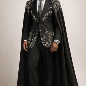 Puede incluir: Un traje negro con capa a juego, adornado con brillantes detalles plateados. El traje incluye una camisa blanca, una corbata gris y un pa&ntilde;uelo de bolsillo. El conjunto se completa con zapatos negros y un reloj de pulsera plateado.