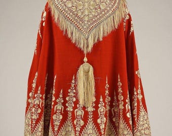 May include: A red cape with intricate gold embroidery and fringe. The cape features a detailed floral pattern along the hem and a decorative embroidered collar. A long tassel hangs from the back of the cape, adding to its ornate design.