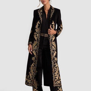 May include: A black velvet duster coat with gold embroidered floral patterns. The coat features a long, flowing design with ornate detailing along the edges and sleeves. The outfit includes matching black pants and a black shirt.