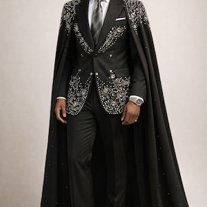 Puede incluir: Traje negro con capa, adornado con pedrer&iacute;a plateada. El traje incluye camisa blanca, corbata gris y pa&ntilde;uelo de bolsillo. La capa larga y los zapatos negros completan el conjunto. Ideal para eventos formales.