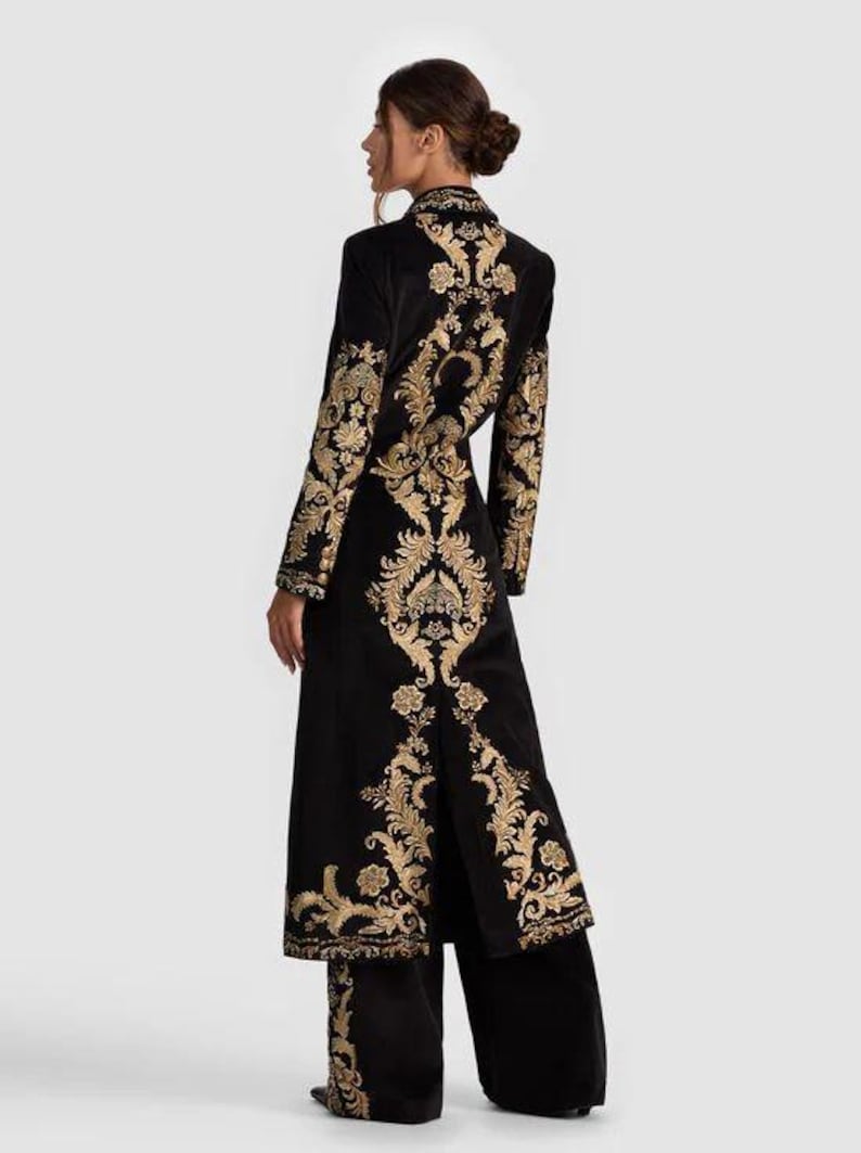 May include: Black velvet coat and matching pants set with gold floral embroidery. The long coat features a high collar and a split back. The gold embroidery is on the sleeves, back, and pant legs. The outfit is elegant and suitable for special occasions.