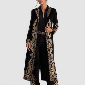 May include: A black velvet duster coat with gold embroidered floral patterns. The coat features a long, flowing design with ornate detailing along the edges and sleeves. The outfit includes matching black pants and a black shirt.