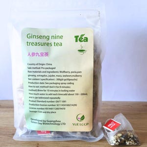 May include: A white resealable pouch of ginseng nine treasures tea with a tea bag inside. The pouch has a green label with the text "Ginseng nine treasures tea" and "人参九宝茶" in Chinese characters. The label also includes information about the ingredients, country of origin, and storage instructions.