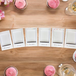 Könnte beinhalten: Ein Set mit acht Fotobox-Requisiten für eine Bridal Shower oder eine Hochzeit. Die Requisiten sind mit Sätzen wie "I Do Crew", "Bride Squad" und "She's Getting Hitched" bedruckt. Die Requisiten sind von rosafarbenen Cupcakes umgeben.