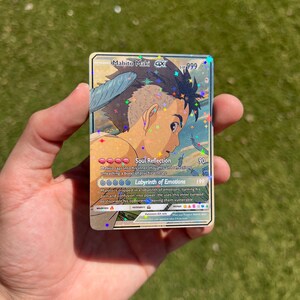 Puede incluir: Una carta de Pok&eacute;mon hologr&aacute;fica con Mahito Maki, un personaje con cabello azul y un atuendo azul y blanco. La carta tiene un fondo azul claro con estrellas y un efecto hologr&aacute;fico. El texto de la carta dice "Reflexi&oacute;n del alma" y "Laberinto de emociones".