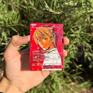 May include: A rectangular trading card featuring a holographic red background with a character illustration of Light Yagami. The card displays the text Light Yagami EX, 230 HP, Kira's Judgment ability, and Death Note attack with 200 damage.