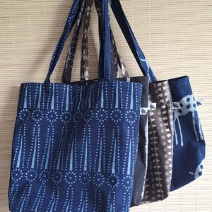 Puede incluir: Cuatro bolsas de mano con asas de tela cuelgan frente a una persiana de bambú marrón claro. Las bolsas presentan varios patrones azules y marrones, incluyendo líneas verticales con puntos y un diseño punteado. Las bolsas son de tela.