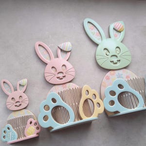May include: Easter-themed wooden decorations featuring bunny faces and paw-shaped holders in pastel colors. The bunnies have floral patterned ears and decorative egg accents. The set includes pink, green, and yellow elements.