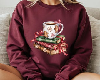 May include: Burgundy sweatshirt with a festive design. A white mug with coffee, gingerbread men, and snowflakes sits on a stack of books tied with red ribbons. The books are green and brown with snowflake details.