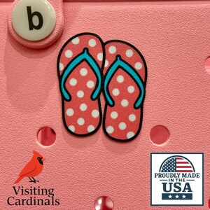 May include: Pink background with a pair of red and white polka dot flip flops with blue straps. The text "Proudly Made in the USA" is below the flip flops.