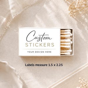 May include: A white box of custom stickers with the text "Custom Stickers" in a script font. The box is open, revealing sticker labels. The labels measure 1.5 x 2.25 inches.