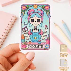 May include: A colourful sticker depicting a skeleton crafter with blue and pink hair, holding scissors and a flower. The sticker has a floral border and the text "THE CRAFTER". The sticker is on a white surface.