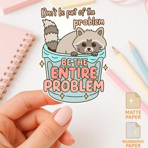 May include: A sticker with a cartoon raccoon in a blue container, with the text "Don't be part of the problem, Be the entire problem." The design includes gold stars and is available in matte, holographic, and glossy paper options.