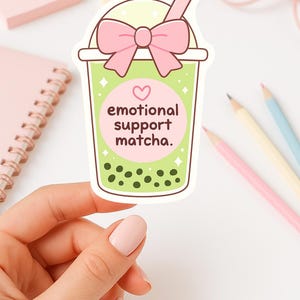 Puede incluir: Una pegatina con una ilustraci&oacute;n de dibujos animados de una bebida de matcha boba. La bebida est&aacute; en un vaso transparente con un lazo rosa, una pajita rosa y las palabras "emotional support matcha". La bebida tiene l&iacute;quido verde y boba verde oscuro.