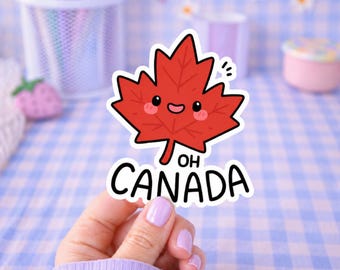 May include: A red maple leaf sticker with a smiling face and the text "OH CANADA" in black. The sticker has a white border and is held up by a hand with purple nail polish. The background is a blue and white checkered pattern.