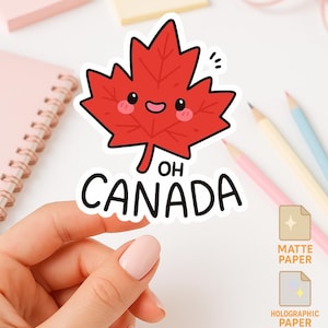 May include: A red maple leaf sticker with a smiling face and the text "OH CANADA". The sticker is held by a hand, with other stationery items in the background. The sticker options are matte, holographic, and glossy paper.