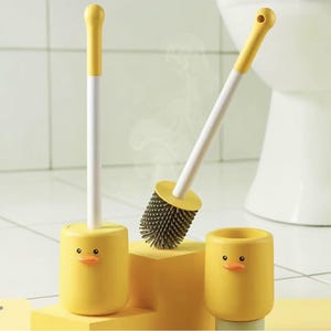 Peut inclure: Ensemble de brosses de toilette sur le thème du canard jaune. L'ensemble comprend une brosse avec un manche jaune et une tige blanche, un support et un petit récipient. La tête de brosse est gris foncé. L'ensemble est conçu pour ajouter une touche ludique à la décoration de la salle de bain.