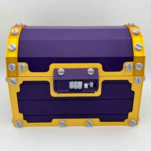 May include: A purple treasure chest with gold trim and silver rivets. The chest has a combination lock on the front. The chest is made of a hard material and has a rectangular shape.