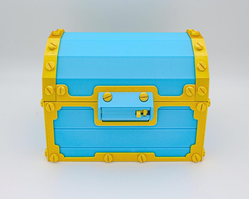 May include: A blue treasure chest with gold-colored trim and hardware. The chest has a rectangular shape with a curved top and a latch on the front. The gold trim is detailed with simulated screw heads.