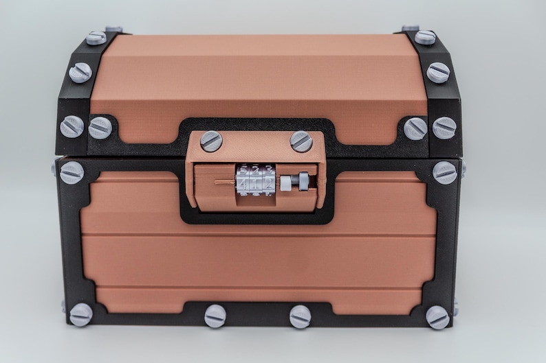May include: A copper-colored chest with black trim and silver-colored screws. The chest has a combination lock and is designed with a classic, vintage aesthetic. The chest is a decorative storage container.