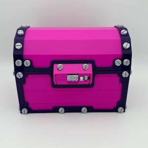 May include: A vibrant pink treasure chest with dark blue trim and silver-colored hardware. The chest features a combination lock and is secured with multiple silver-colored screws. The design is geometric and modern, suggesting a decorative or storage item.