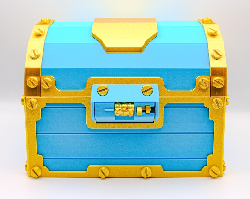 May include: A blue treasure chest with gold-colored accents. The chest features a combination lock and is adorned with decorative screws. The design includes a gold-colored top and trim, creating a striking contrast against the blue body.