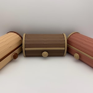 May include: Three wooden bread boxes in shades of tan, brown, and reddish-brown. Each box has a rounded top and a small, round knob. The boxes are made of wooden slats and have a decorative trim.