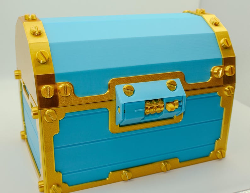 May include: A blue treasure chest with gold-colored trim and accents. The chest features a combination lock and is secured with gold-colored screws. The chest has a rectangular shape with a slightly curved top.