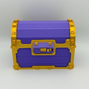 Op de afbeelding: Een paarse schatkist met goudkleurige accenten. De kist heeft een rechthoekige vorm met een gebogen bovenkant en is versierd met goudkleurige schroeven en een slot. Het algehele ontwerp doet denken aan een klassieke schatkist.