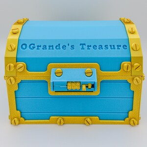 May include: A blue treasure chest with gold-colored accents and the text "OGrande's Treasure" on the lid. The chest has a combination lock and decorative screws. The chest is a decorative storage container.