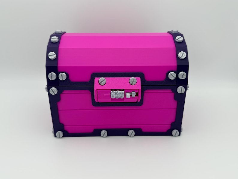May include: A vibrant pink treasure chest with dark blue trim and silver-colored hardware. The chest features a combination lock and is secured with multiple silver-colored screws. The design is geometric and modern, suitable for storage or decoration.