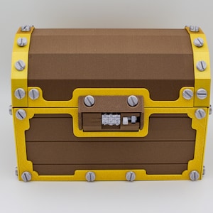 May include: A brown treasure chest with yellow trim and silver screws. The chest has a combination lock and is made of wood-like material. The chest is closed and sits on a white surface.