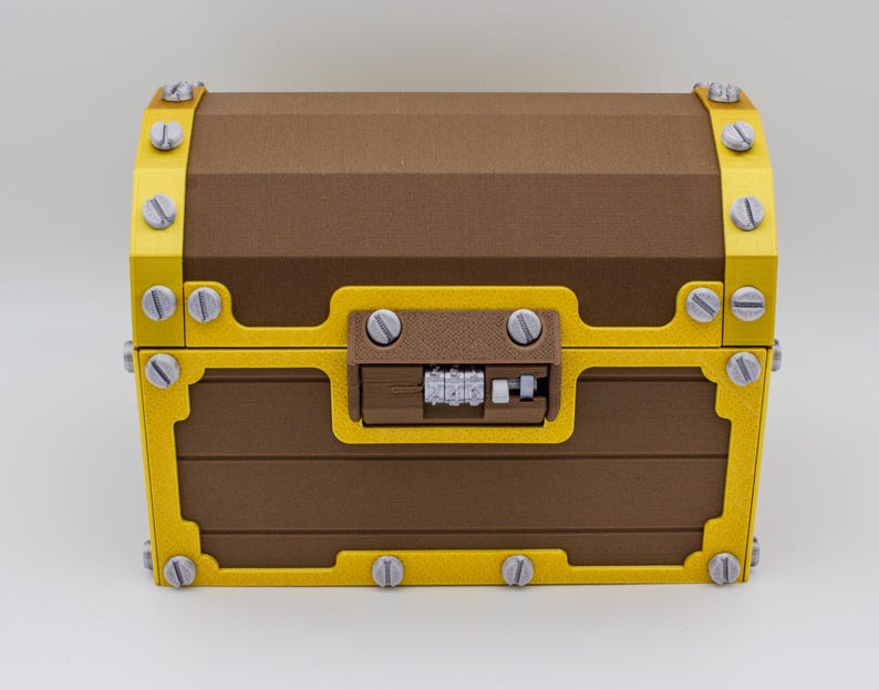 May include: A brown treasure chest with yellow trim and silver screws. The chest has a combination lock and is made of wood-like material. The chest is closed and sits on a white surface.