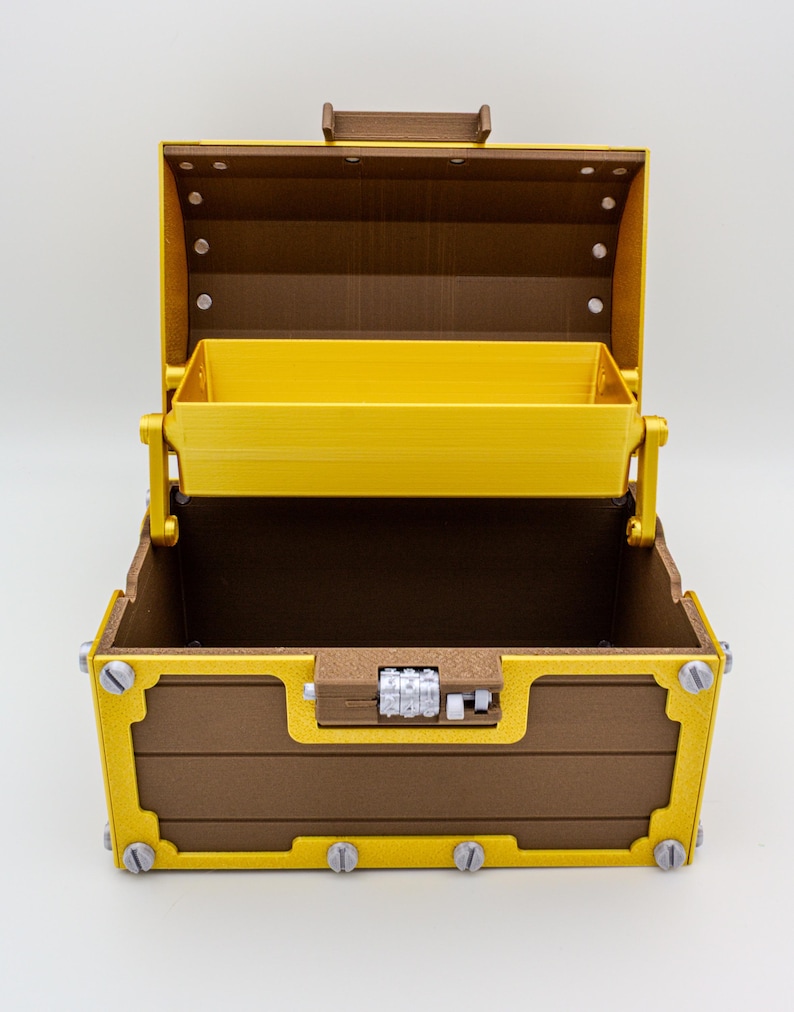 May include: An open, brown and gold treasure chest with a yellow interior. The chest features a combination lock and decorative metal accents. The lid is open, revealing a yellow tray inside.