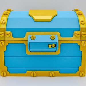 May include: A blue treasure chest with gold-colored accents. The chest features a rectangular shape with a hinged lid and a latch. Gold-colored metal bands and rivets adorn the corners and edges, adding a decorative touch. The chest is a vibrant and eye-catching decorative item.