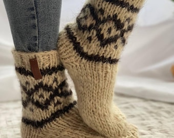 May include: A pair of thick, knitted socks in cream and brown. The socks feature a geometric pattern in dark brown and a leather tag. The socks are worn with blue jeans.