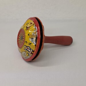 以下が含まれることがあります： 黄色と赤色の塗装が施された、ヴィンテージのおもちゃマラカス。マラカスには漫画のキャラクターと「Zoo-Zoo Products」の文字が描かれています。ハンドルは木製です。
