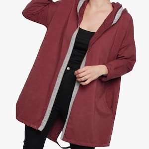 May include: A burgundy hooded jacket with a silver and white trim along the edges and hood. The jacket has a relaxed fit, long sleeves, and pockets. The model is wearing black trousers and a black top.