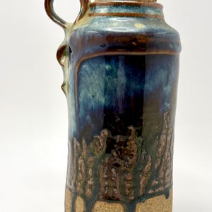 Hand-thrown studio pottery jug with blue-green drip glaze and cork stopper.